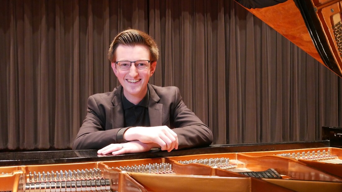 Thomas sitting in front of a piano and smiling
