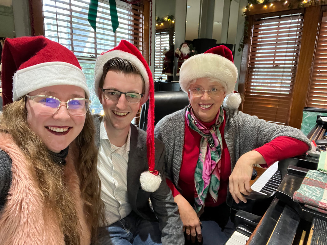 Thomas, Kassidy, and an instructor sitting in front of a piano wearing Santa hats
